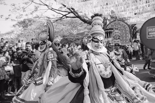 Performers in traditional, elaborate costumes and makeup dancing at an outdoor cultural festival with a crowd watching.